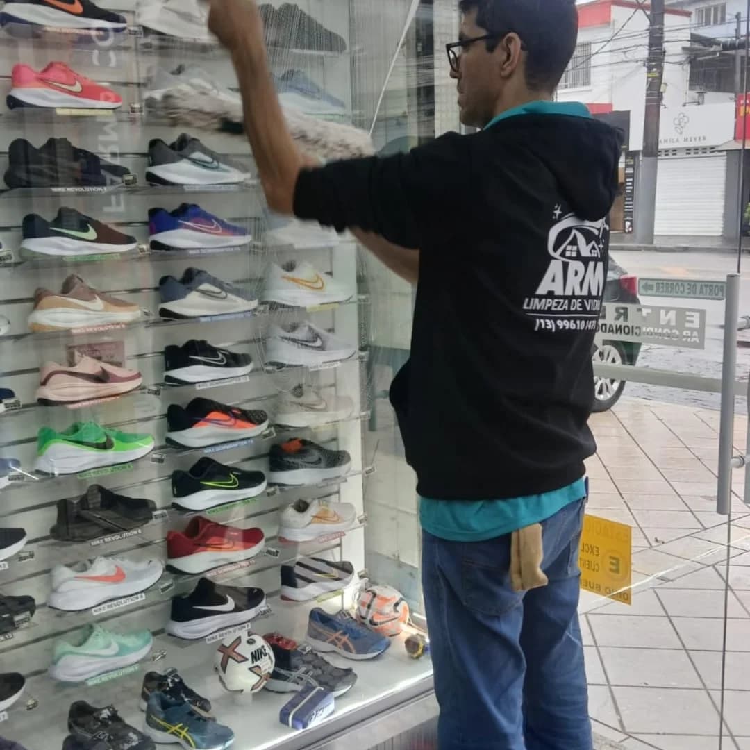 Profissional da ARM limpando a vitrine de uma loja de calçados em Santos